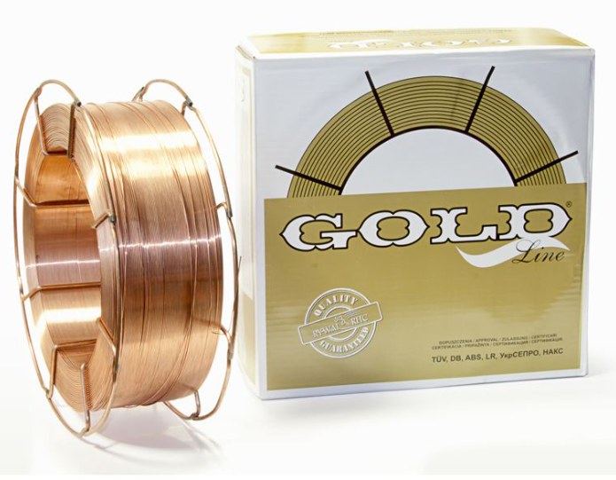 Na zdjęciu znajduje się zwinięta szpulka miedzianego drutu spawalniczego umieszczona obok białego opakowania z napisem GOLD Line oraz grafiką przedstawiającą złoty pierścień. Opakowanie zawiera również oznaczenia jakościowe i certyfikaty TÜV, DB, ABS, LR oraz inne, widoczne na przedniej części kartonu.